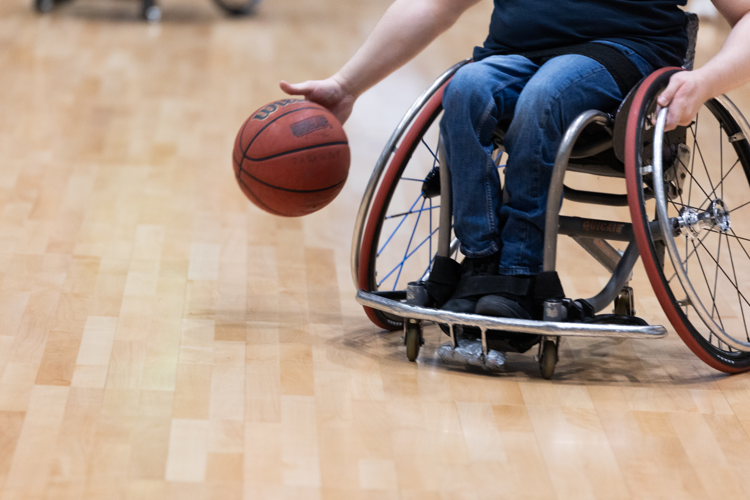 Kuvassa henkilö pompottaa koripalloa koripallokentällä pyörätuolista käsin.